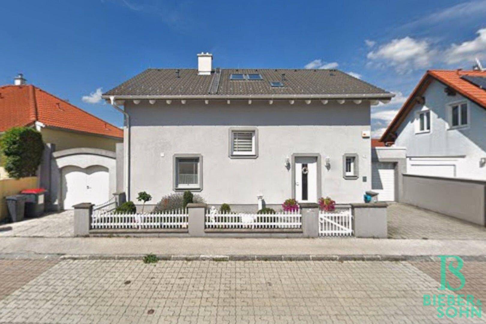 Frontansicht des Einfamilienhauses mit Vorgarten, Garage und gepflasterter Einfahrt.