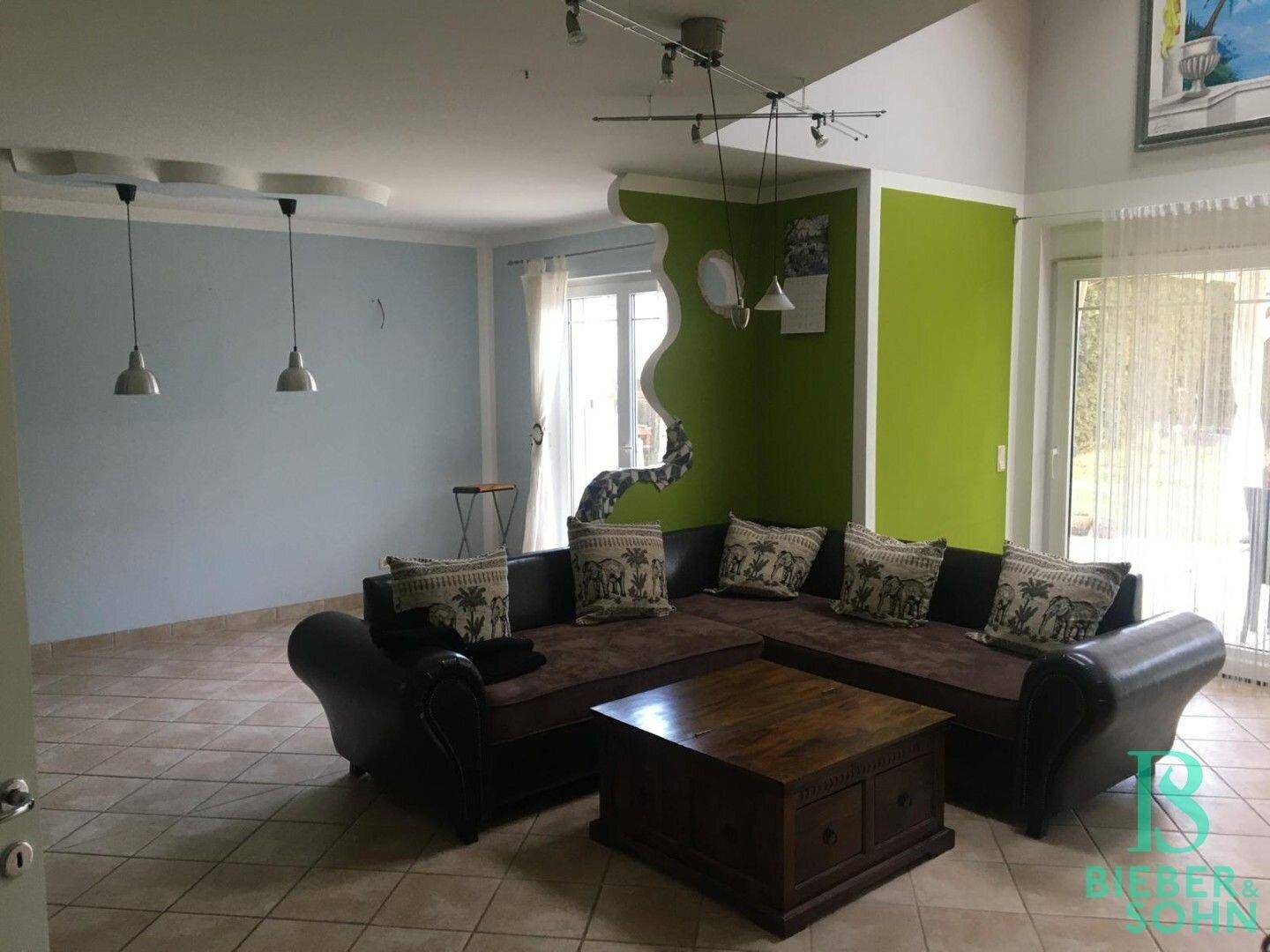Geräumiges Wohnzimmer mit Fliesenboden, Ecksofa und farbigen Wänden in Grün und Hellblau.