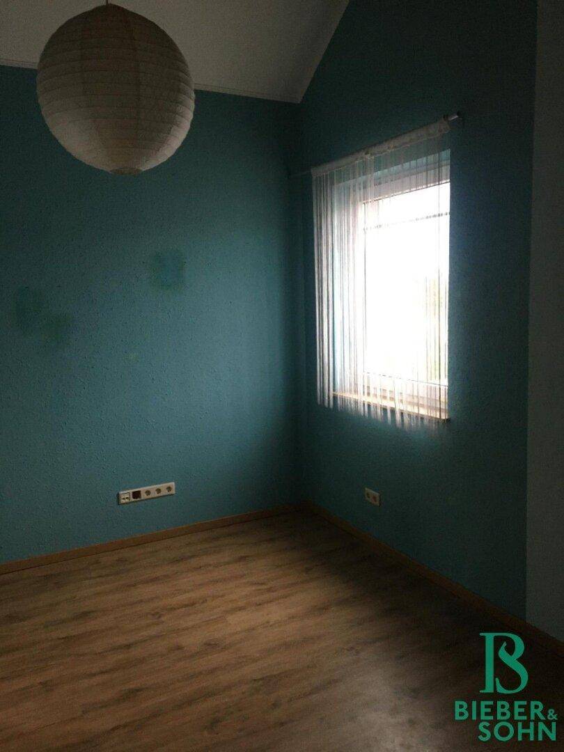 Schlafzimmer mit türkisfarbenen Wänden, Holzboden und einem Fenster mit Vorhang.