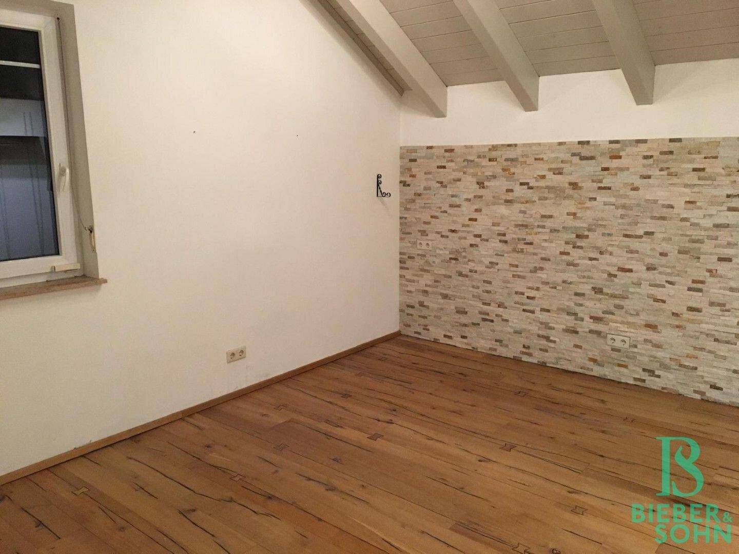 Zimmer mit Holzboden, weiß gestrichenen Wänden und einer dekorativen Steinwand.