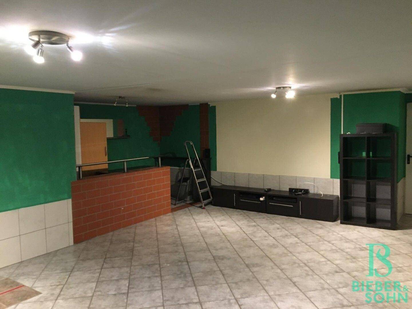 Großer Kellerraum mit Fliesenboden, grünen Wänden und einer Ziegelstein-Bar.