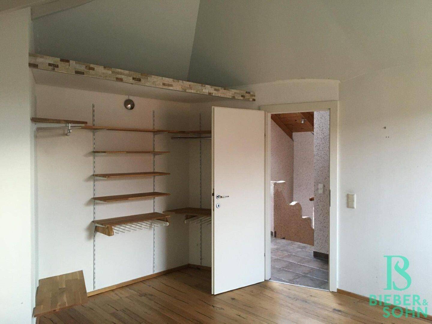 Begehbarer Kleiderschrank mit Regalsystem und Holzboden im Dachgeschoss.