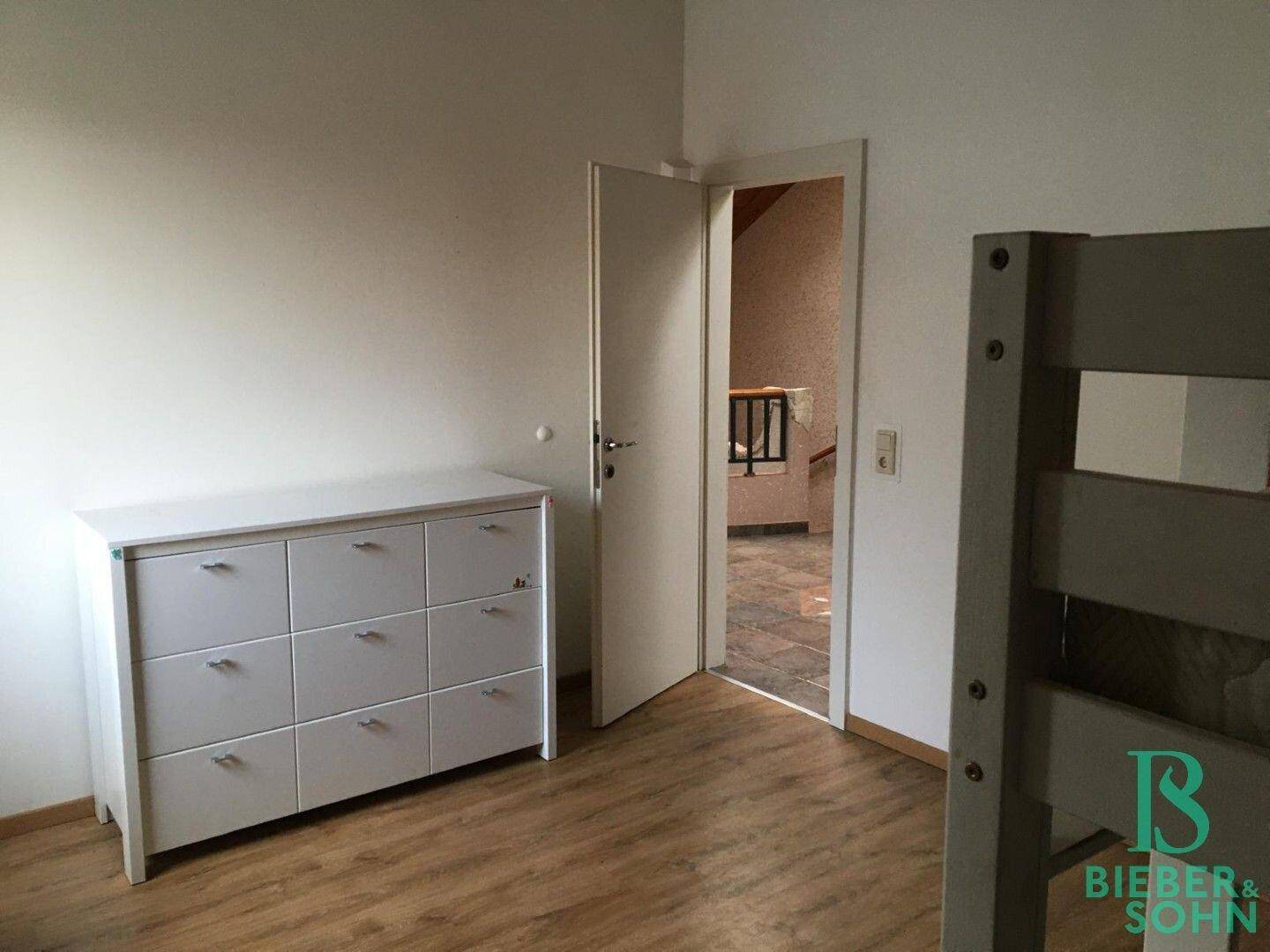 Helles Schlafzimmer im Dachgeschoss mit Kommode und Zugang zum Flur.