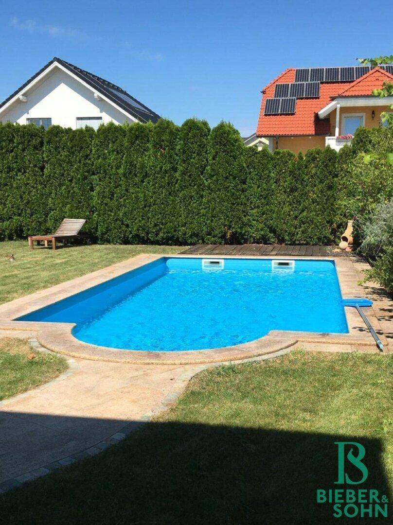Blauer Swimmingpool im Garten, umgeben von Rasen und einer hohen Hecke.