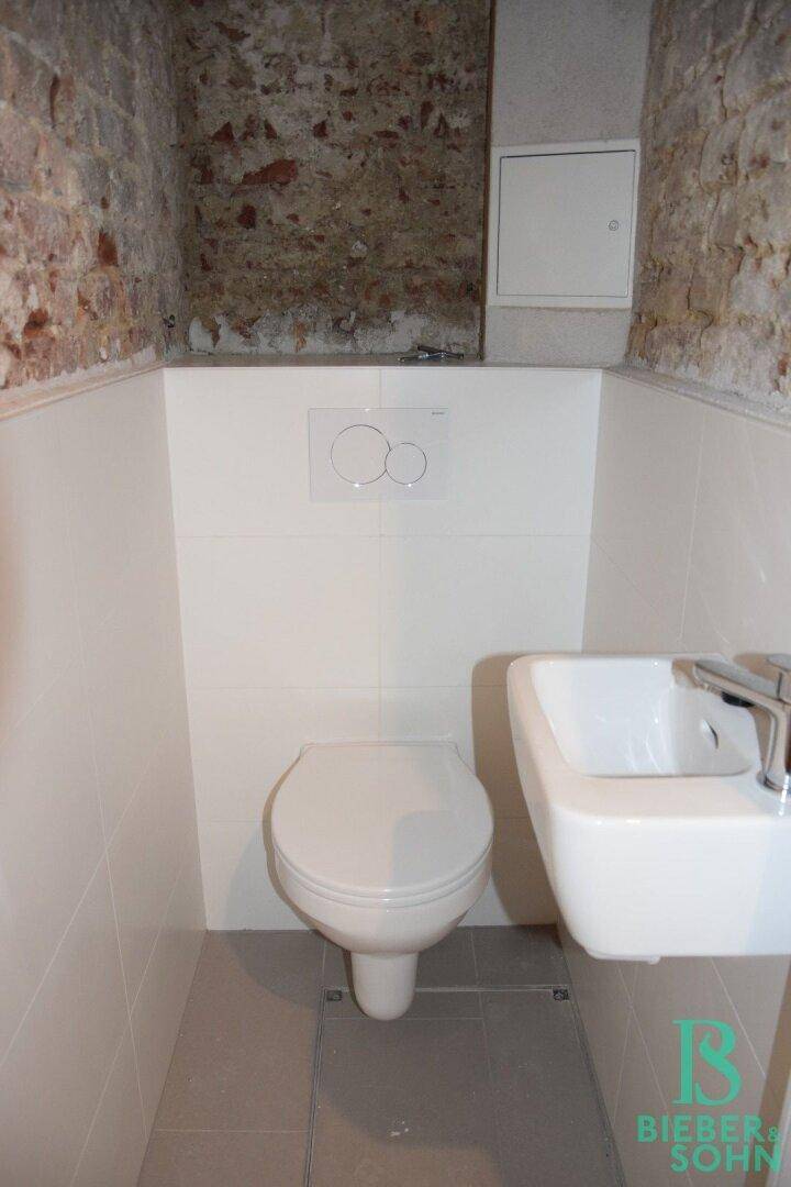 Moderne Toilette mit wandhängendem WC, kleinem Waschbecken und weißen Fliesen an den Wänden.