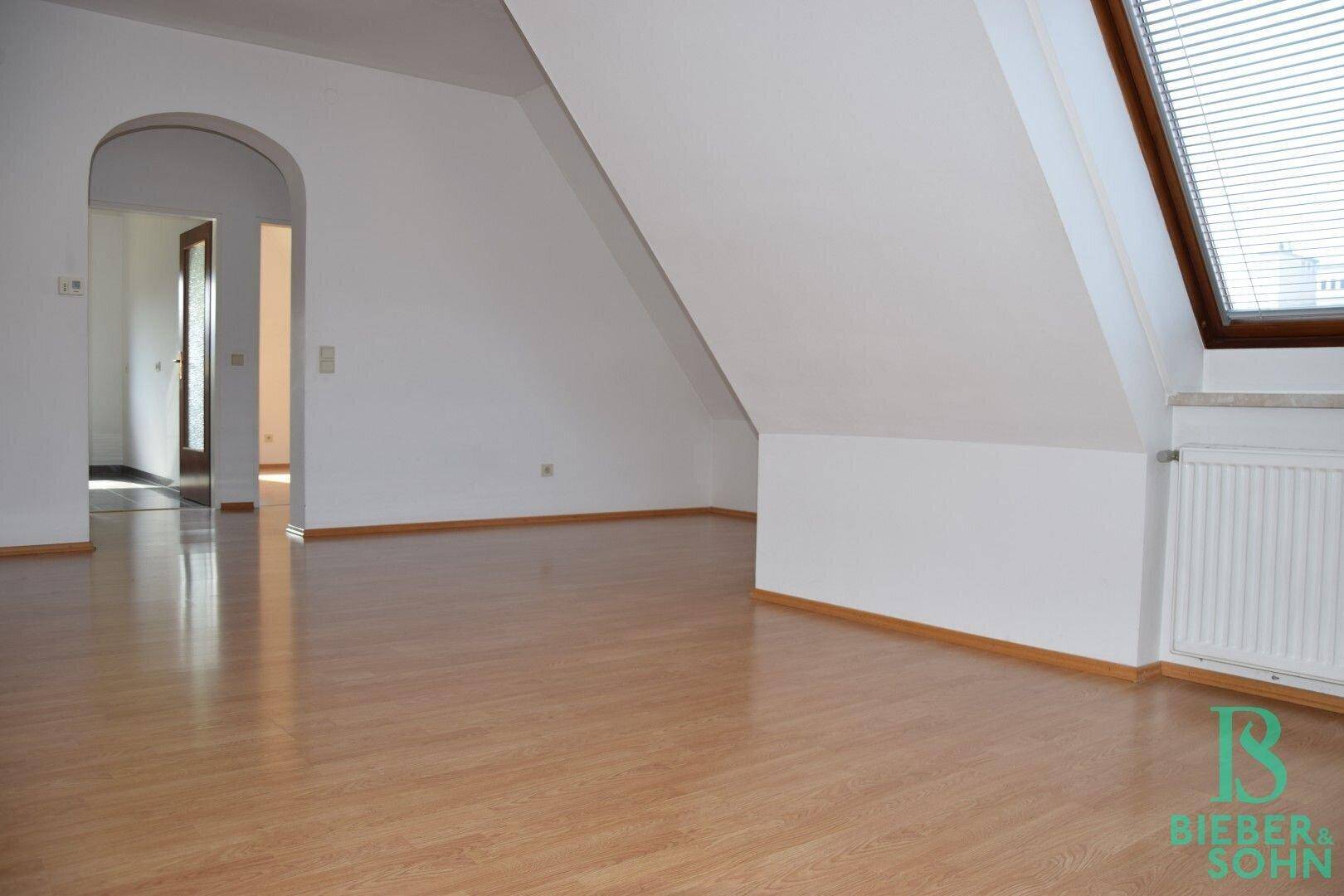 Heller Dachgeschossraum mit Laminatboden, Dachschräge und Blick auf einen weiteren Raum durch einen Bogen.