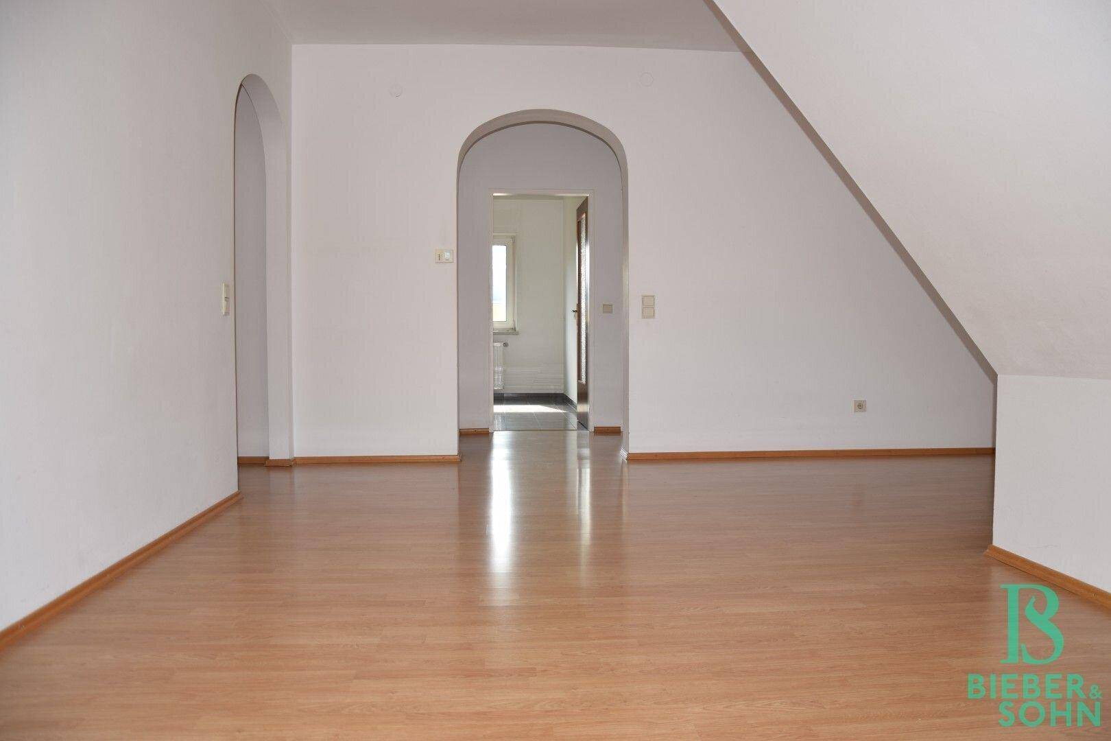Großer Dachgeschossraum mit Laminatboden und zwei Bögen, die zu weiteren Bereichen führen.