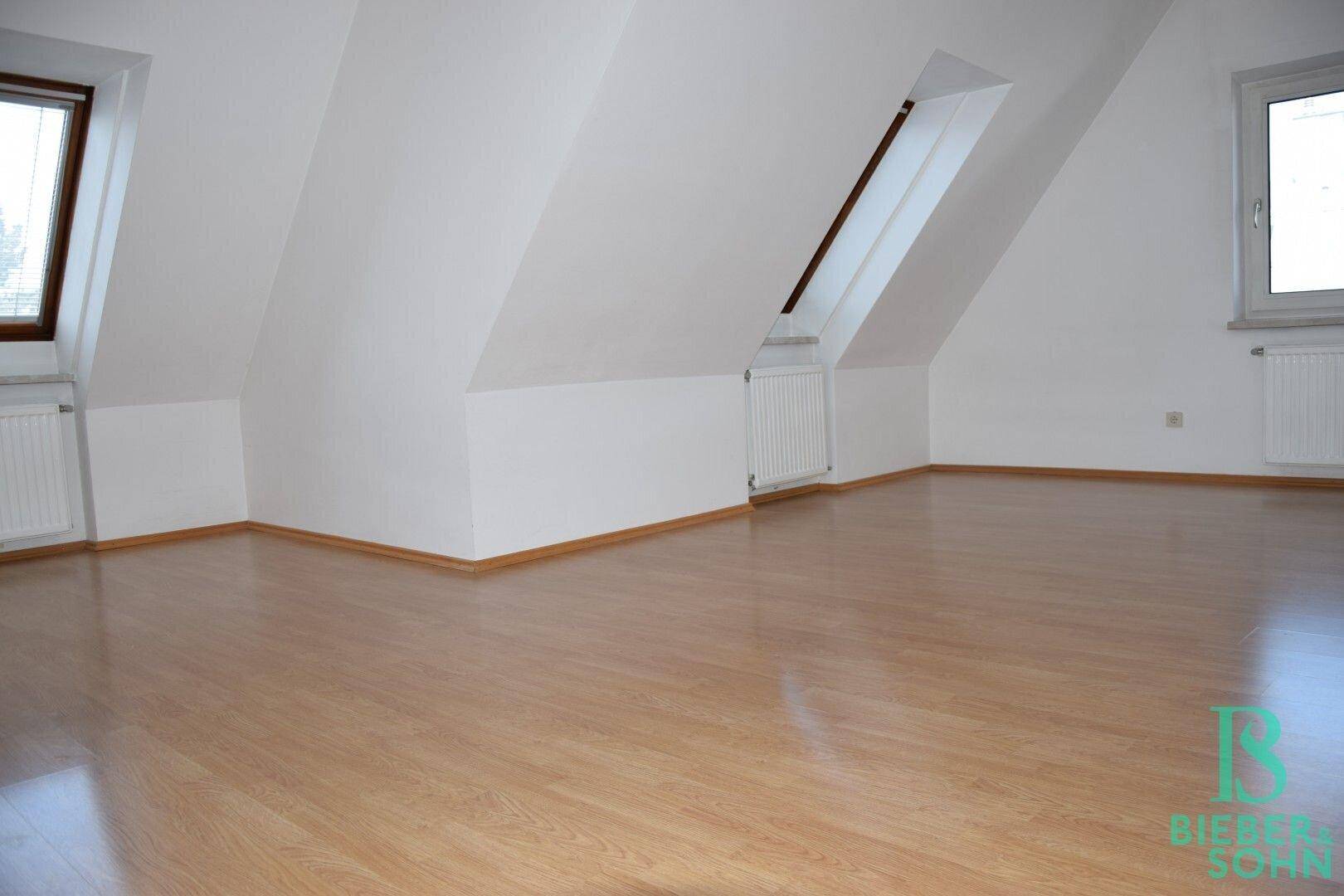 Geräumiger Dachgeschossraum mit Laminatboden, Dachschrägen und mehreren Fenstern für viel Licht.