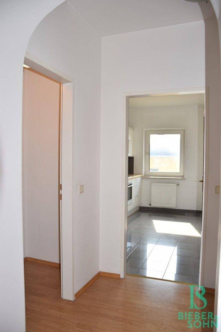Heller Flur mit Laminatboden, der in eine geflieste Küche mit Fenster führt.