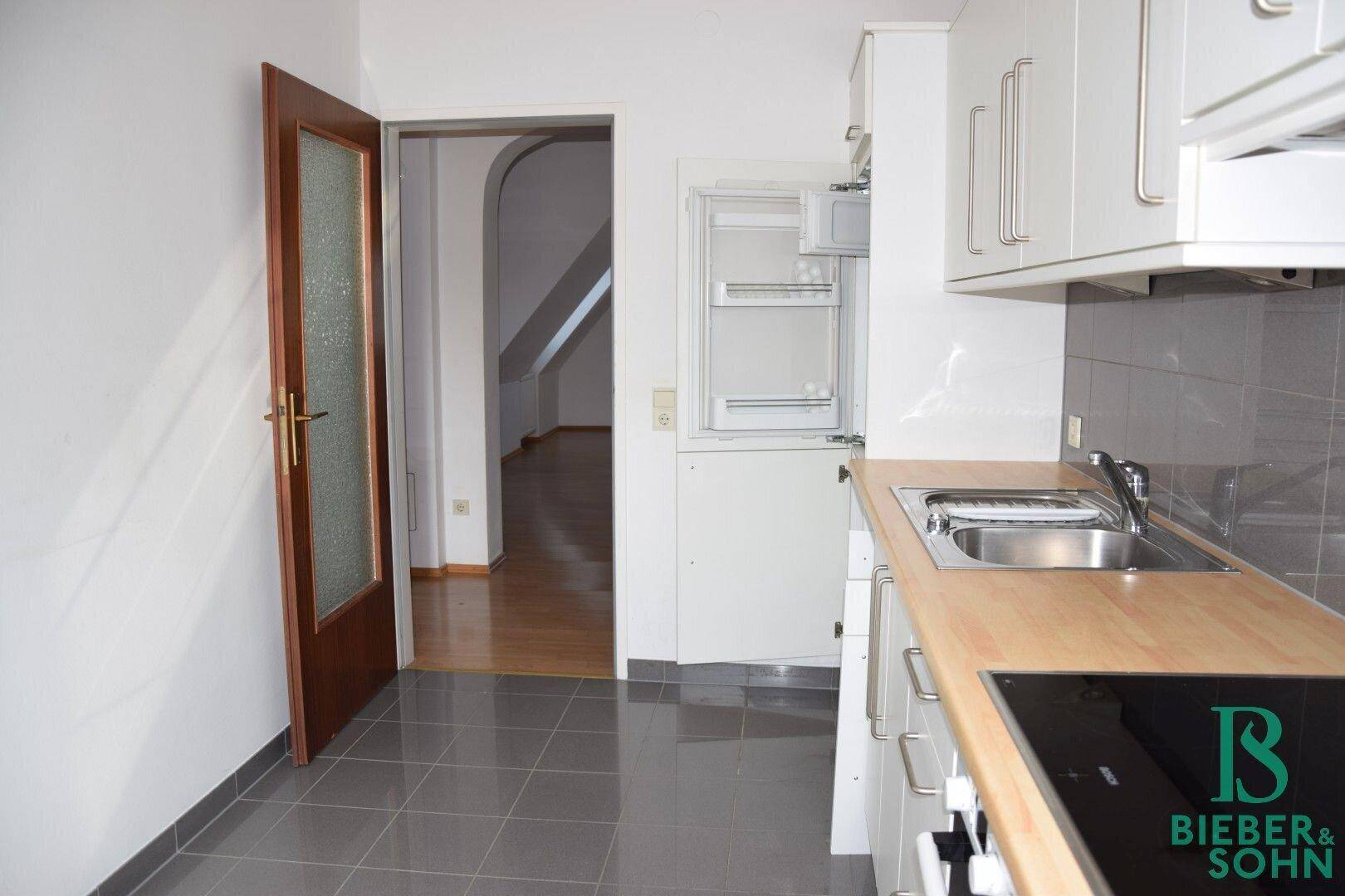 Funktionale Küche mit Fliesenboden und Zugang zu einem weiteren Raum mit Holzboden.