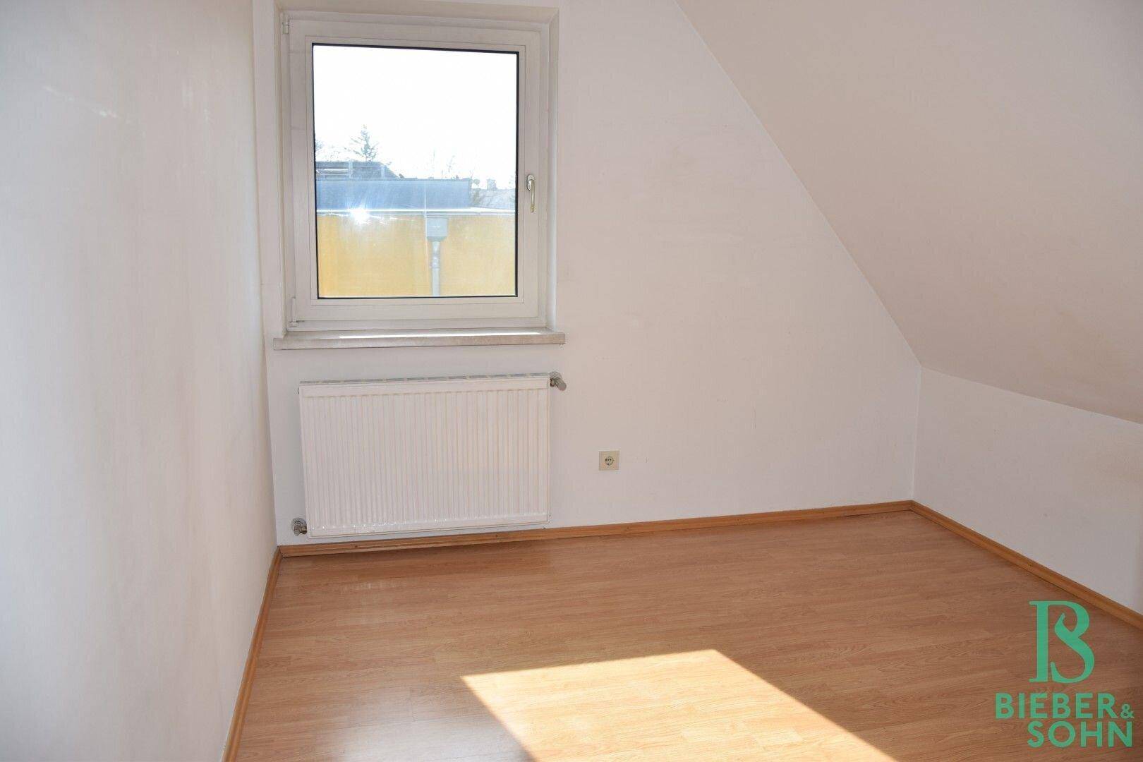 Heller Dachgeschossraum mit Laminatboden, Dachschräge und einem Fenster.