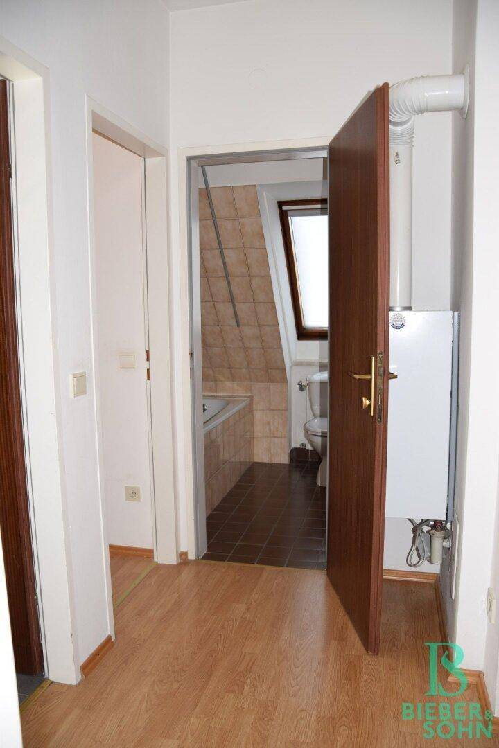 Flur mit Laminatboden und Blick in ein Badezimmer mit Badewanne und Dachfenster.