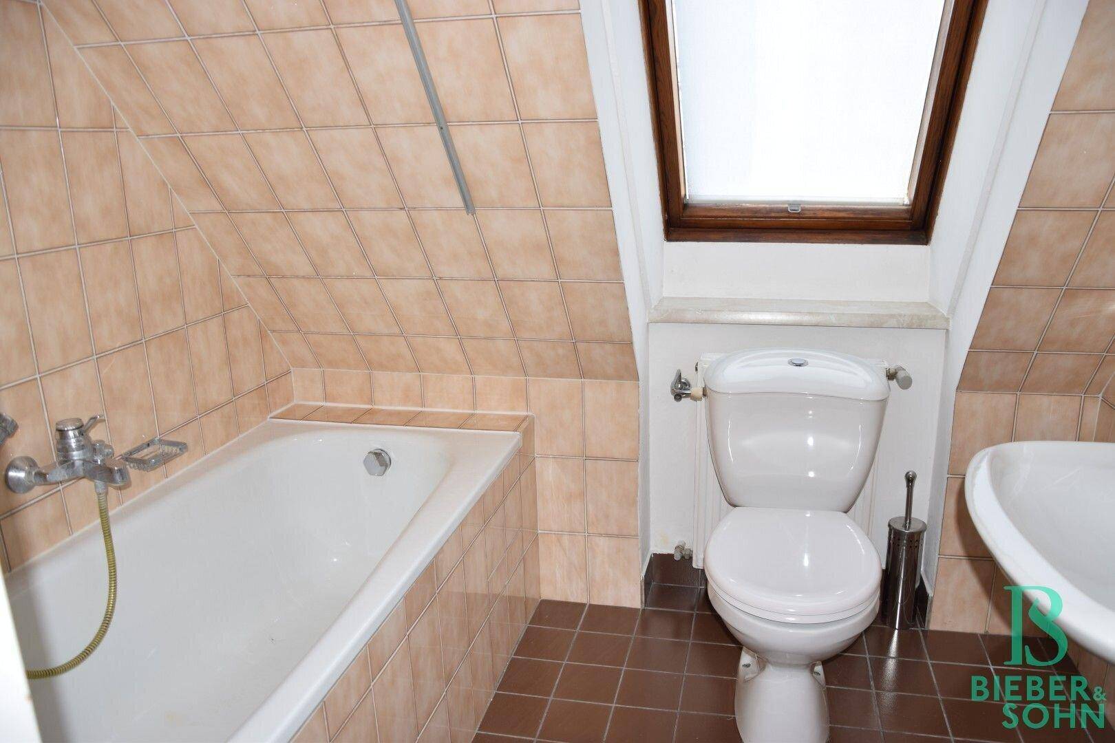 Badezimmer mit Badewanne, Toilette und Dachfenster, komplett gefliest unter der Dachschräge.
