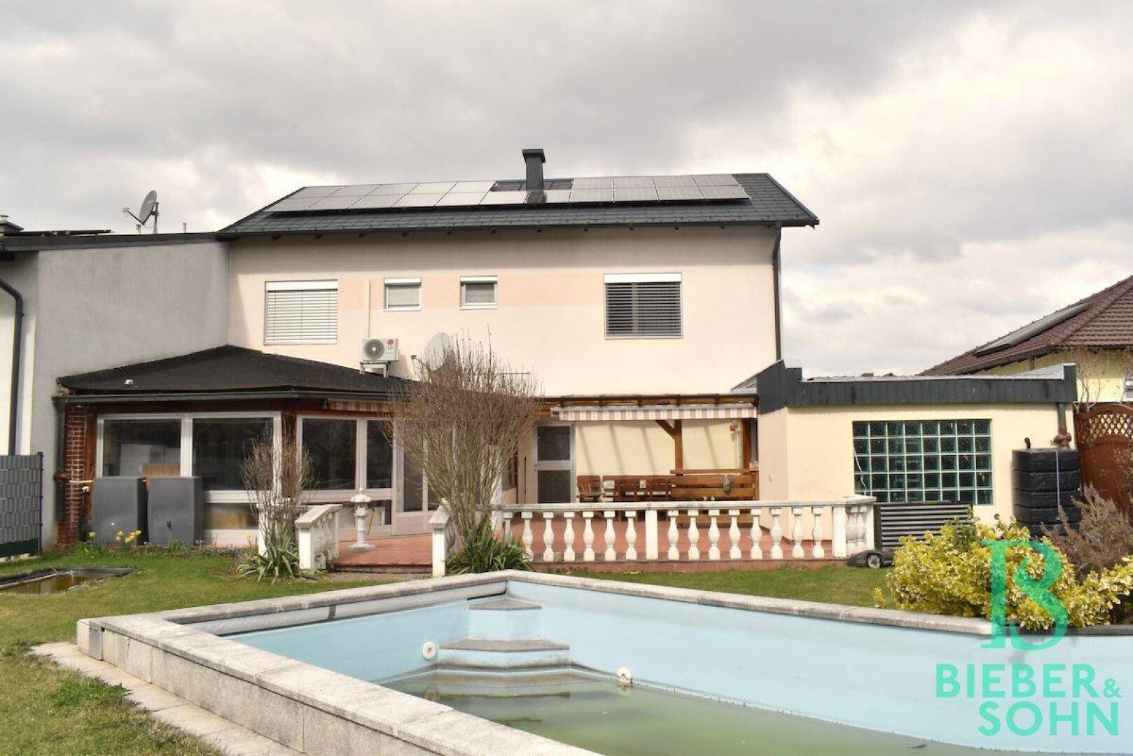 Hinterhof mit eingelassenem Pool und der Rückseite des Hauses mit Solarpaneelen auf dem Dach.