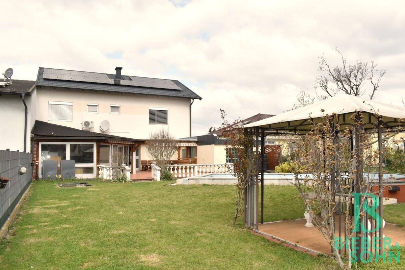 Weitläufiger Gartenbereich mit Rasen, Pool und einer schattenspendenden Gartenlaube.