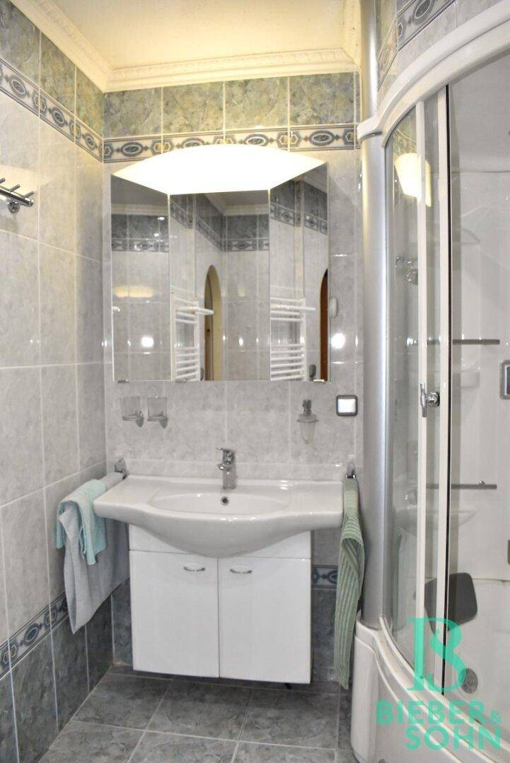 Gefliestes Badezimmer mit Duschkabine, Waschbecken und Spiegelschrank.