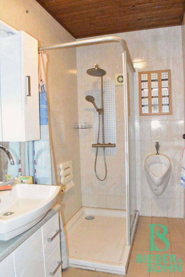 Badezimmer mit Duschkabine, Waschbecken und einem Urinal an der Wand.