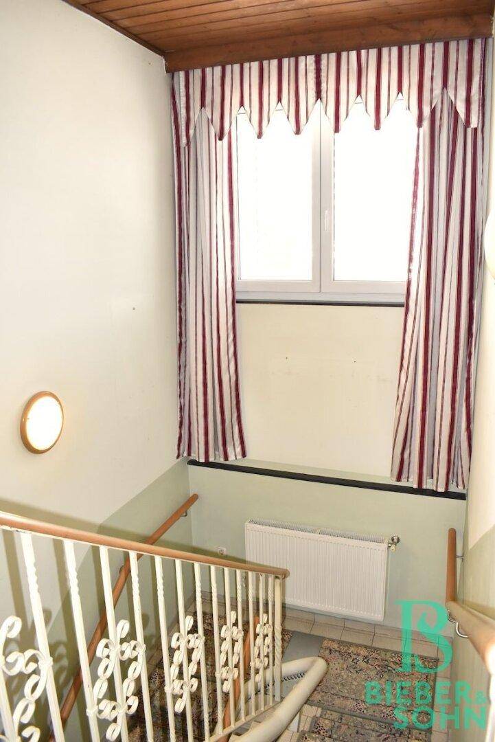 Helles Treppenhaus mit Fenster, Heizkörper und einem verzierten Geländer.