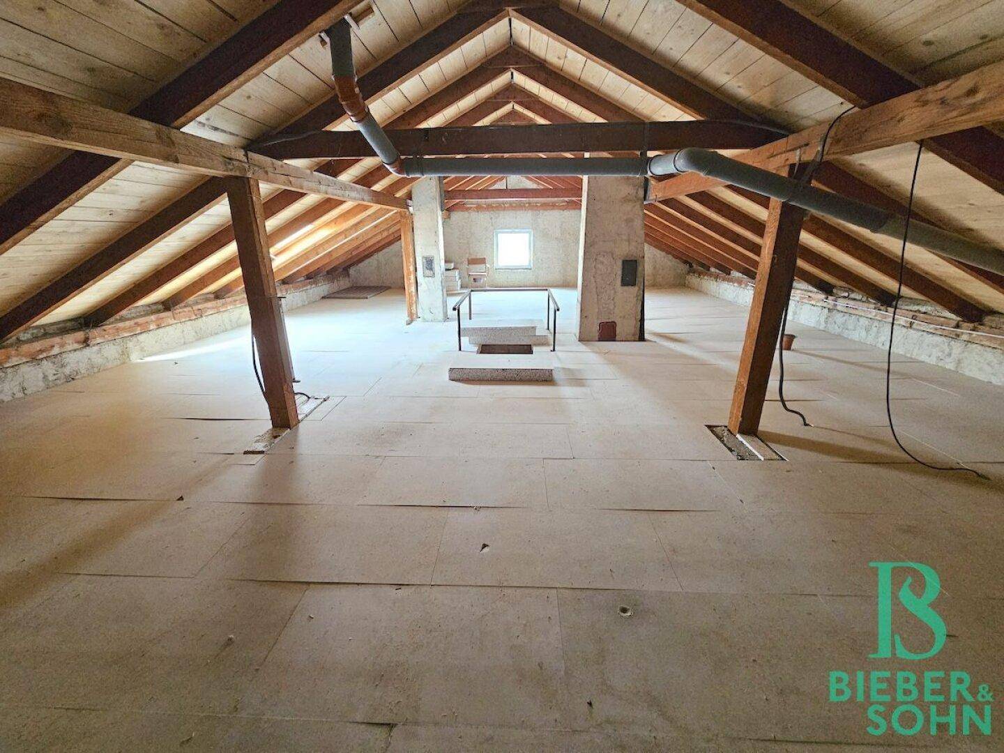 Geräumiger, unausgebauter Dachboden mit sichtbaren Holzbalken und einem kleinen Fenster.