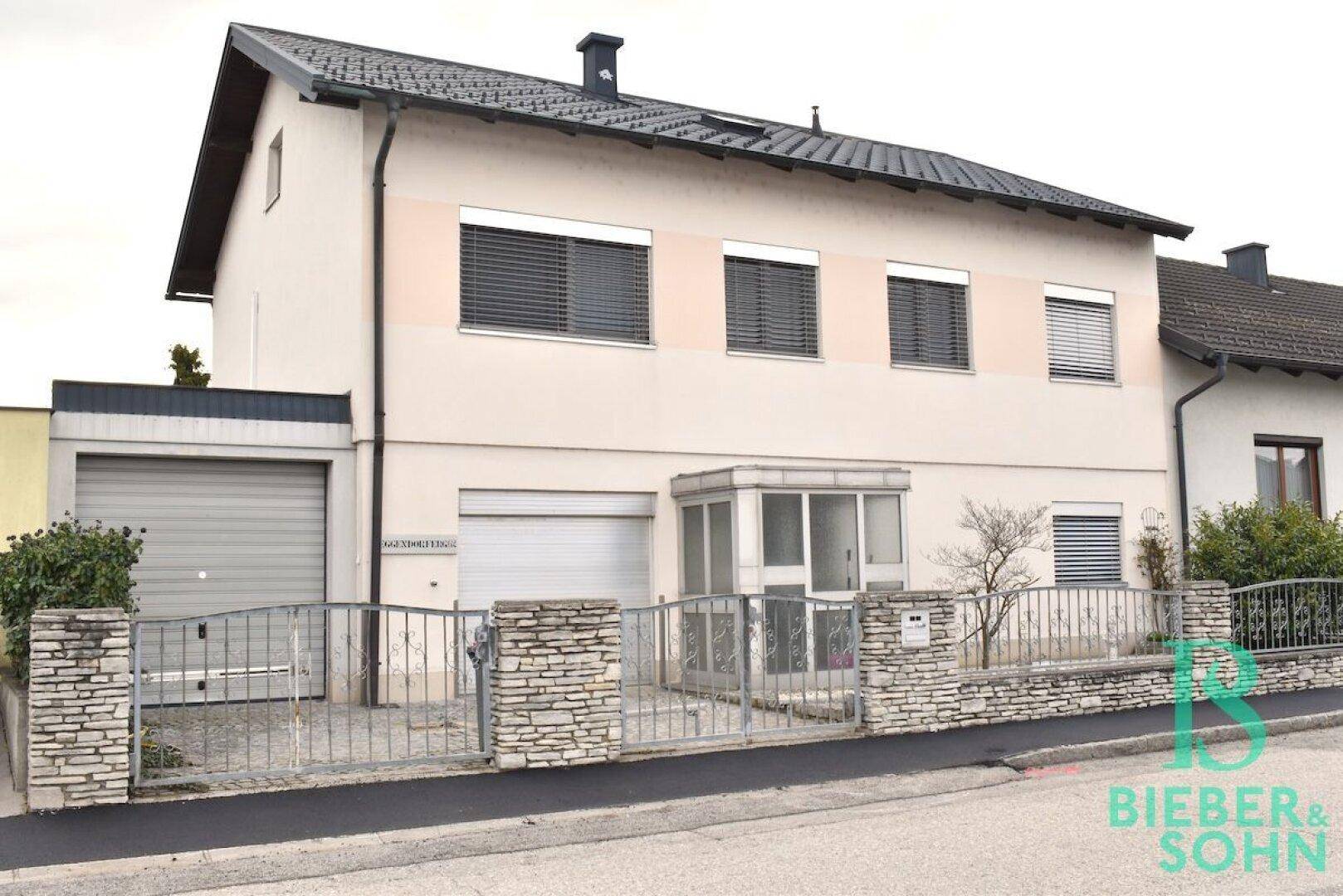 Vorderansicht des Hauses von der Straße mit Garage, Vorgarten und Steinmauer.