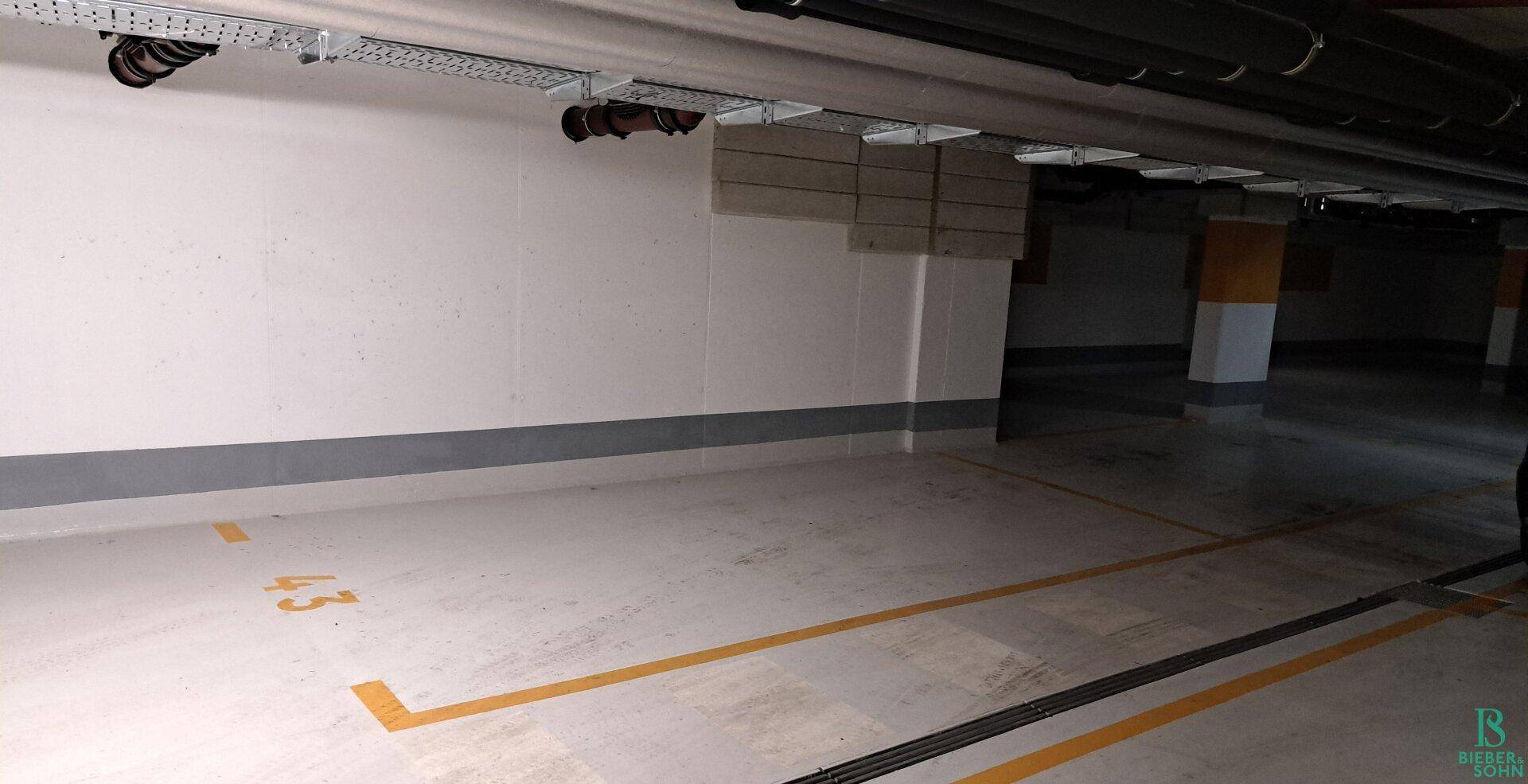 Weiterer Blick in die Tiefgarage mit nummerierten Parkplätzen und Deckeninstallationen.