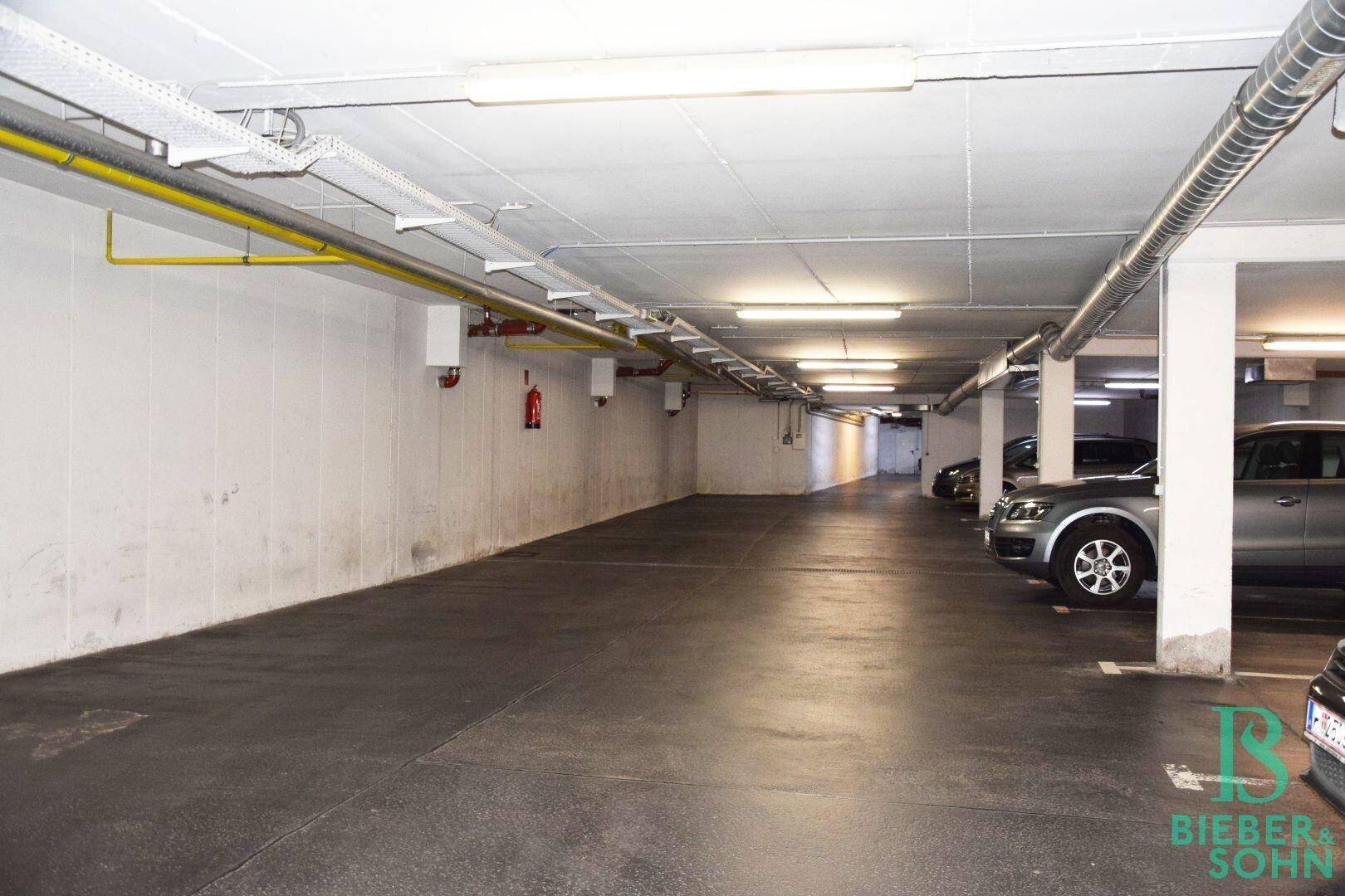 Geräumige Tiefgarage mit mehreren Stellplätzen, Betonwänden und sichtbaren Installationen an der Decke.