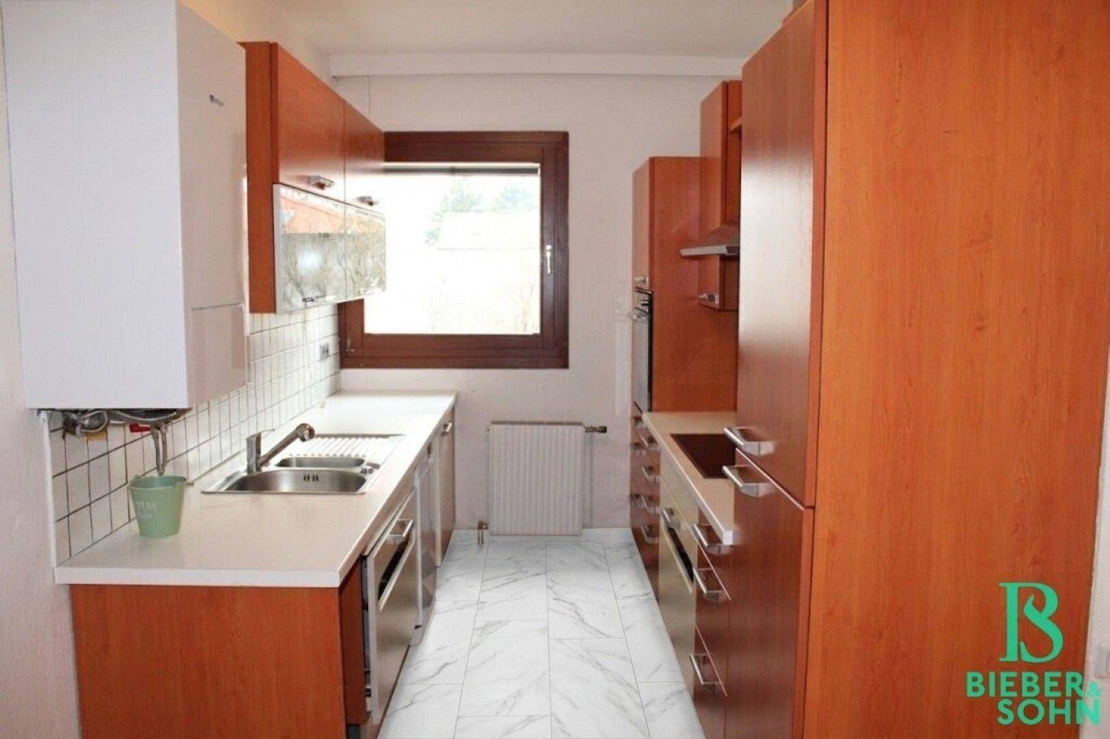 Funktionale Küche mit Holzschränken, weißen Arbeitsplatten und Fliesenboden.