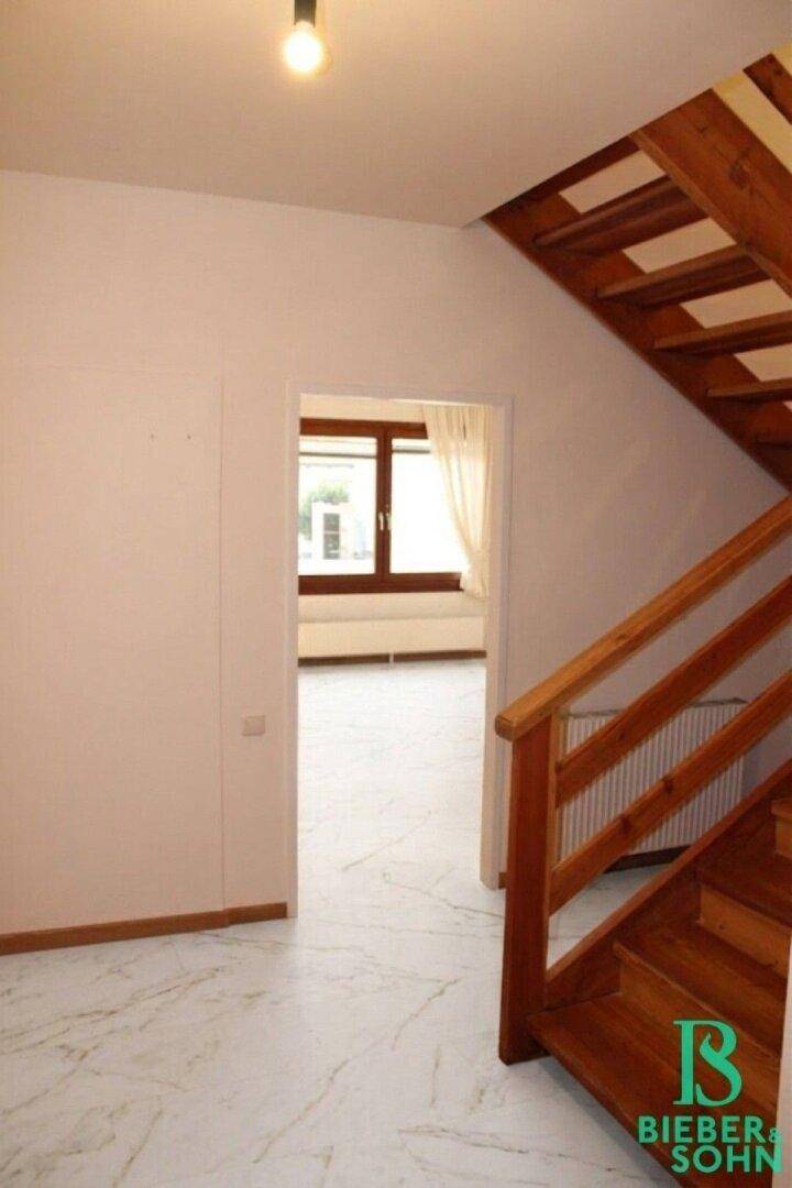 Heller Flur mit Holztreppe und Blick in einen angrenzenden Raum.