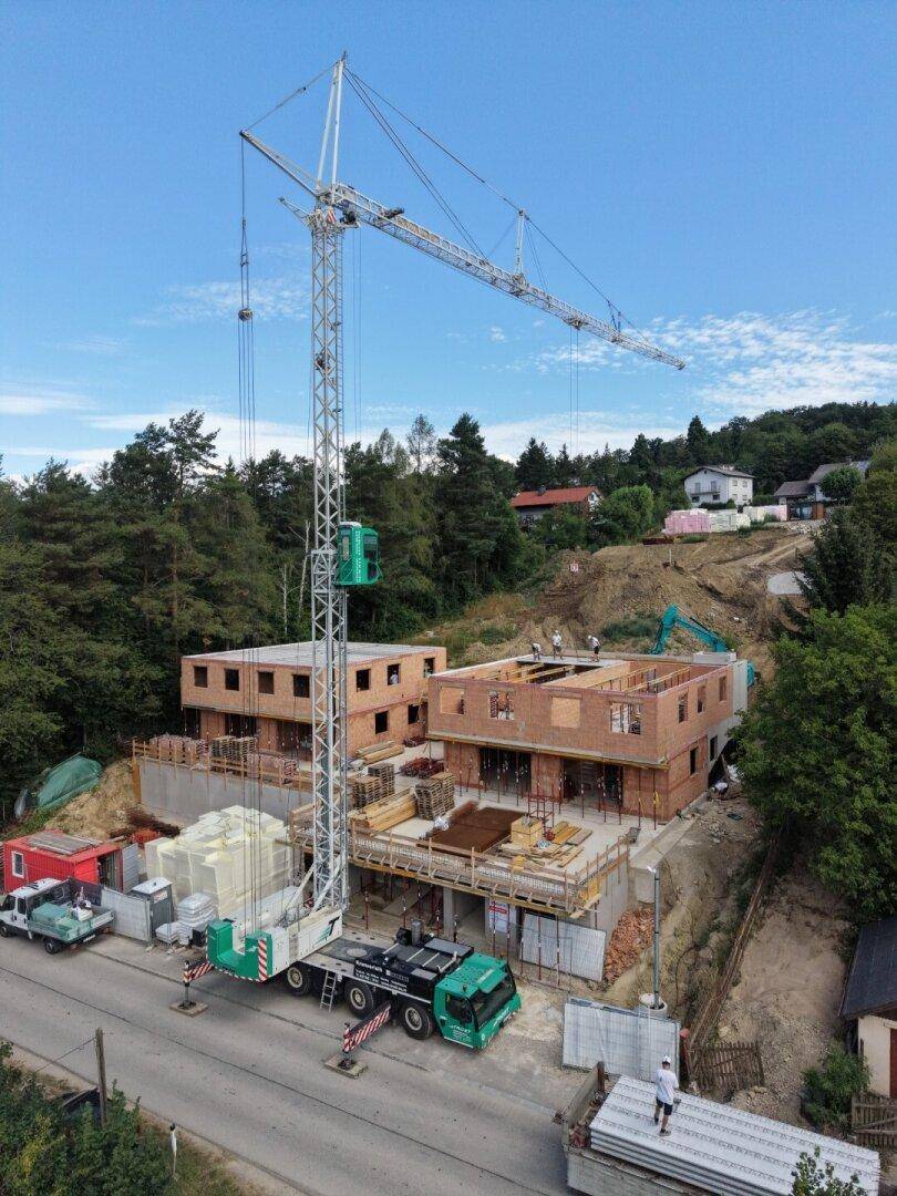Luftaufnahme einer Baustelle mit großem Kran, mehreren Rohbauten und umliegender Natur.