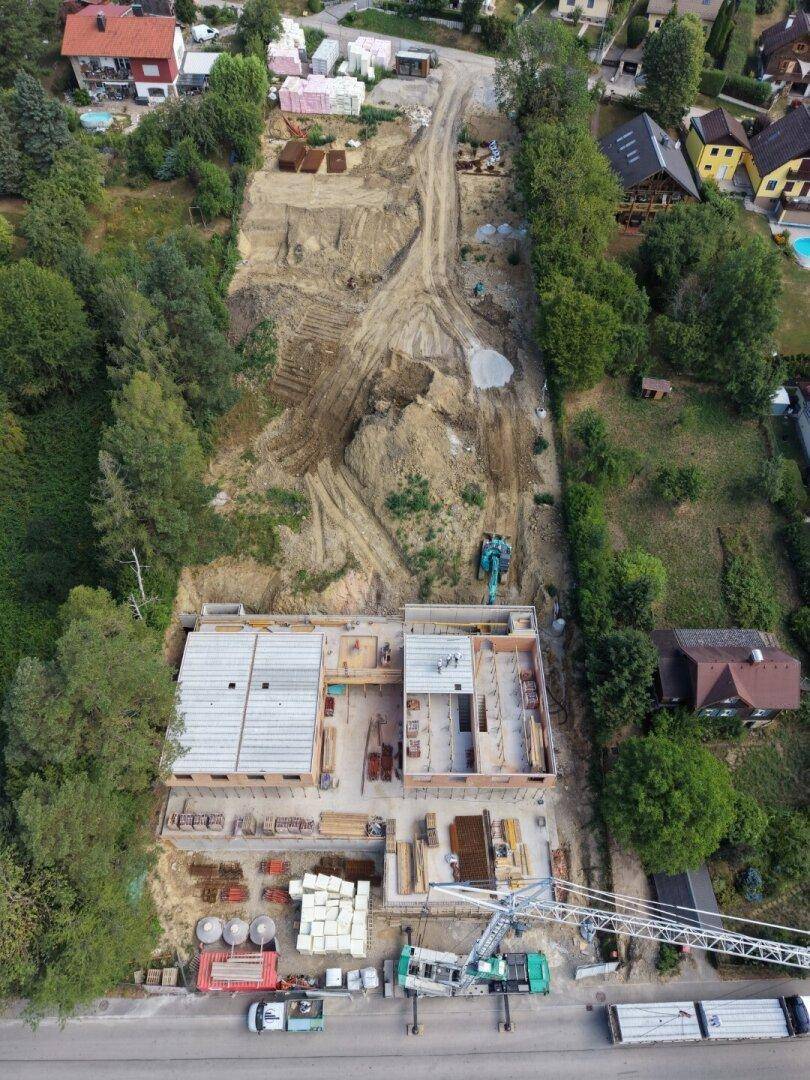 Vogelperspektive einer ausgedehnten Baustelle mit Rohbauten und Erdarbeiten in bewaldeter Umgebung.