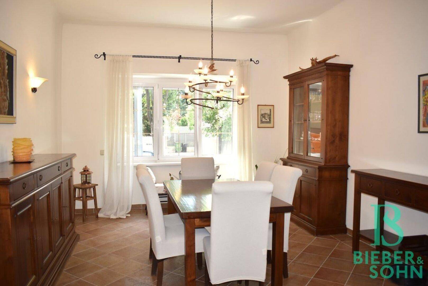 Gemütliches Esszimmer mit Holztisch, traditionellen Möbeln und Blick in den Garten durch ein großes Fenster.