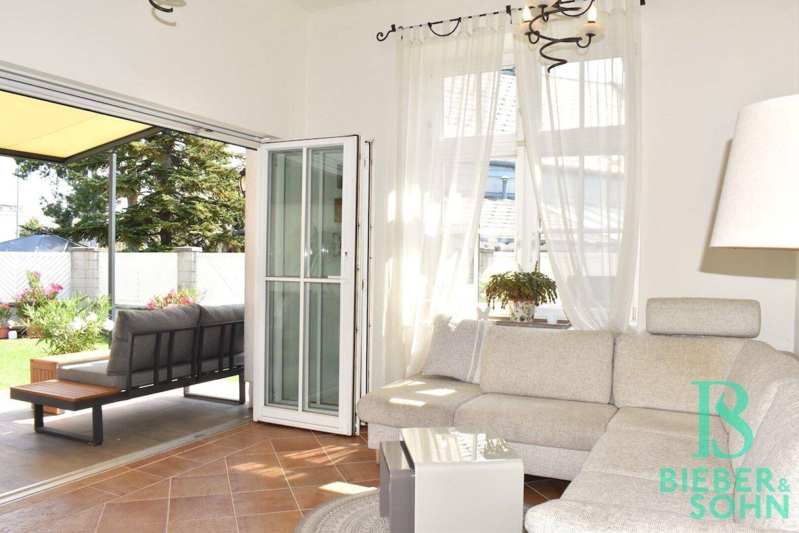 Lichtdurchflutetes Wohnzimmer mit offenem Zugang zur Terrasse und Blick auf den gepflegten Garten.