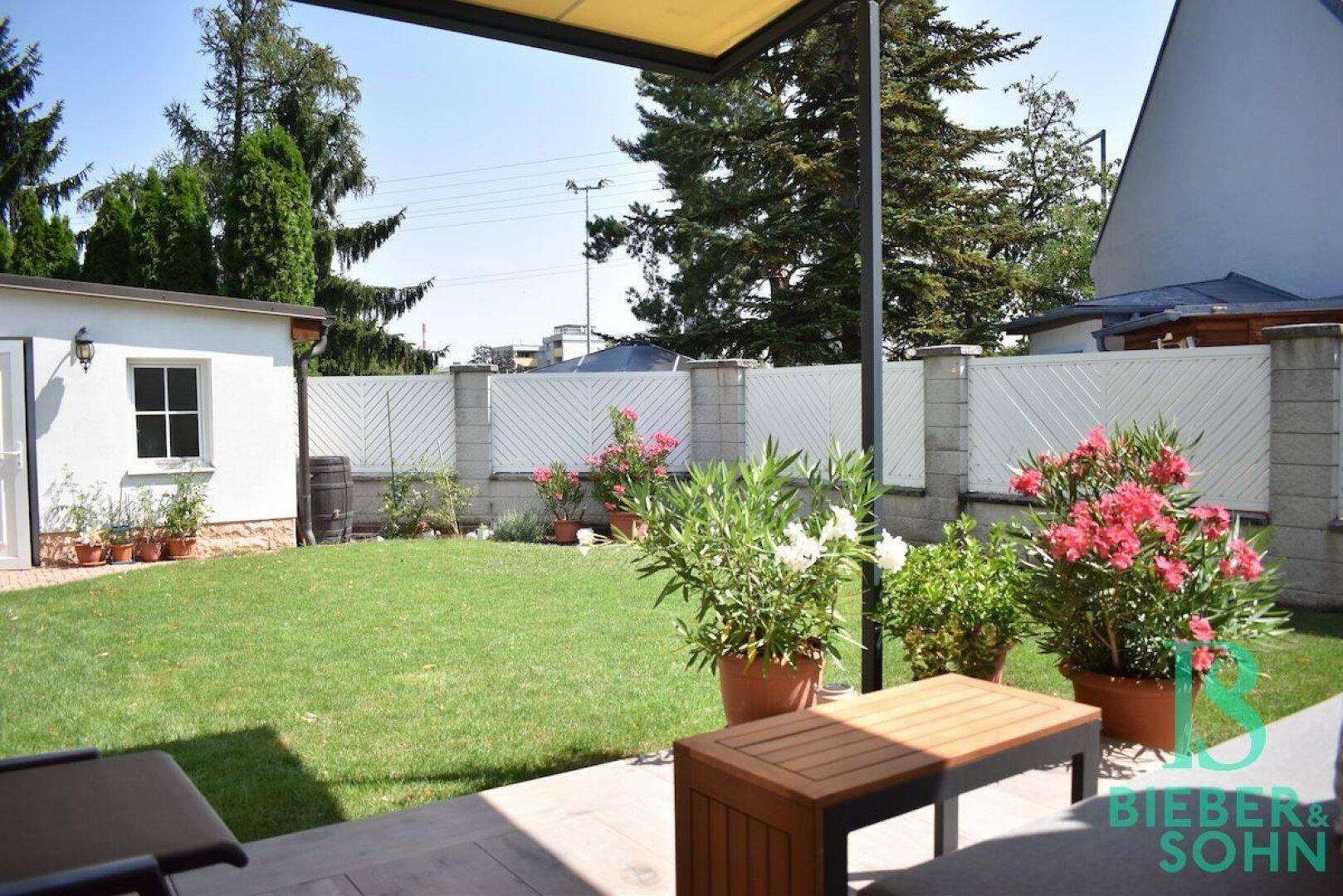 Gepflegter Gartenbereich mit Rasenfläche, blühenden Pflanzen und einer gemütlichen Sitzgelegenheit im Freien.
