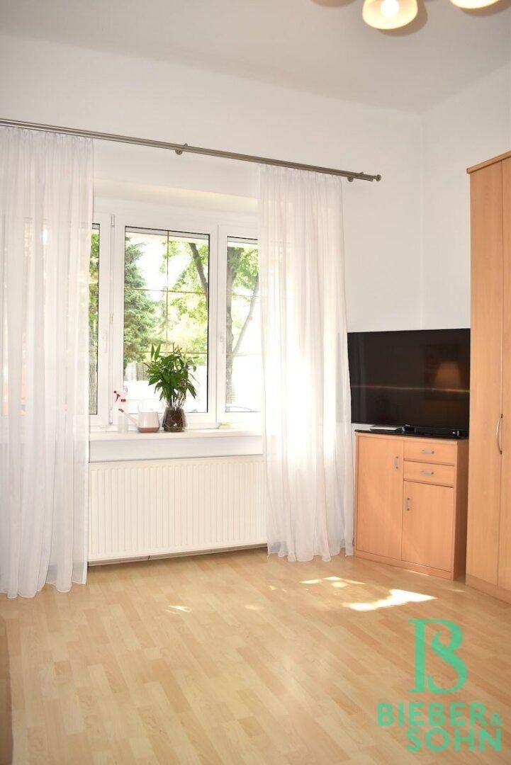 Helles Schlafzimmer mit Laminatboden, großem Fenster und Blick ins Grüne, ausgestattet mit einem Schrank.