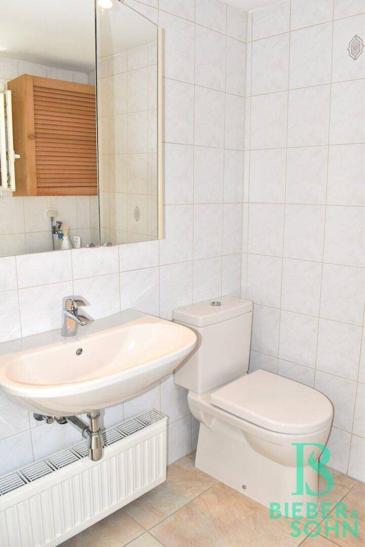 Funktionales WC mit weißen Fliesen, Waschbecken und Toilette, ausgestattet mit einem Heizkörper.
