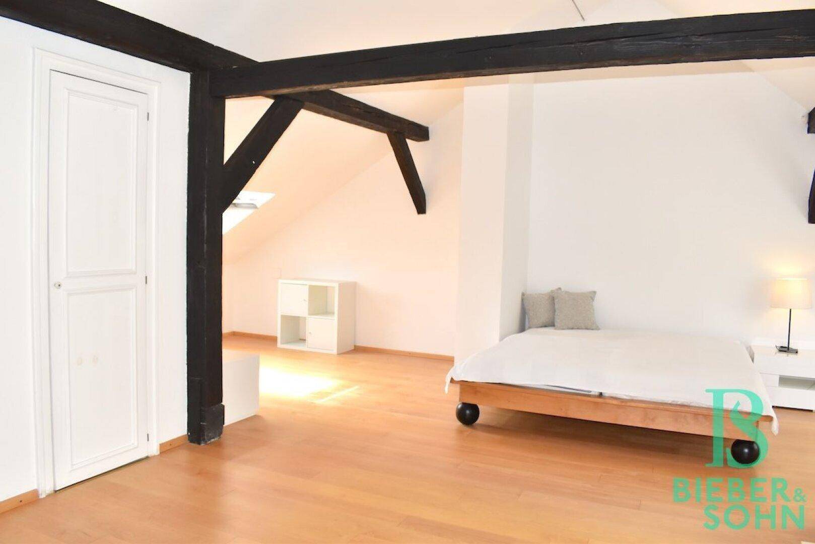 Helles Dachgeschoss-Schlafzimmer mit Holzboden, sichtbaren Balken und praktischem Stauraum.