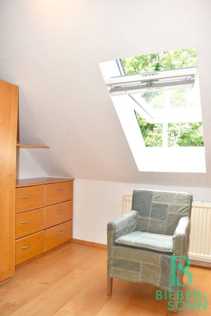 Gemütliche Ecke im Dachzimmer mit Holzschrank, Sessel und einem Dachfenster für viel Licht.