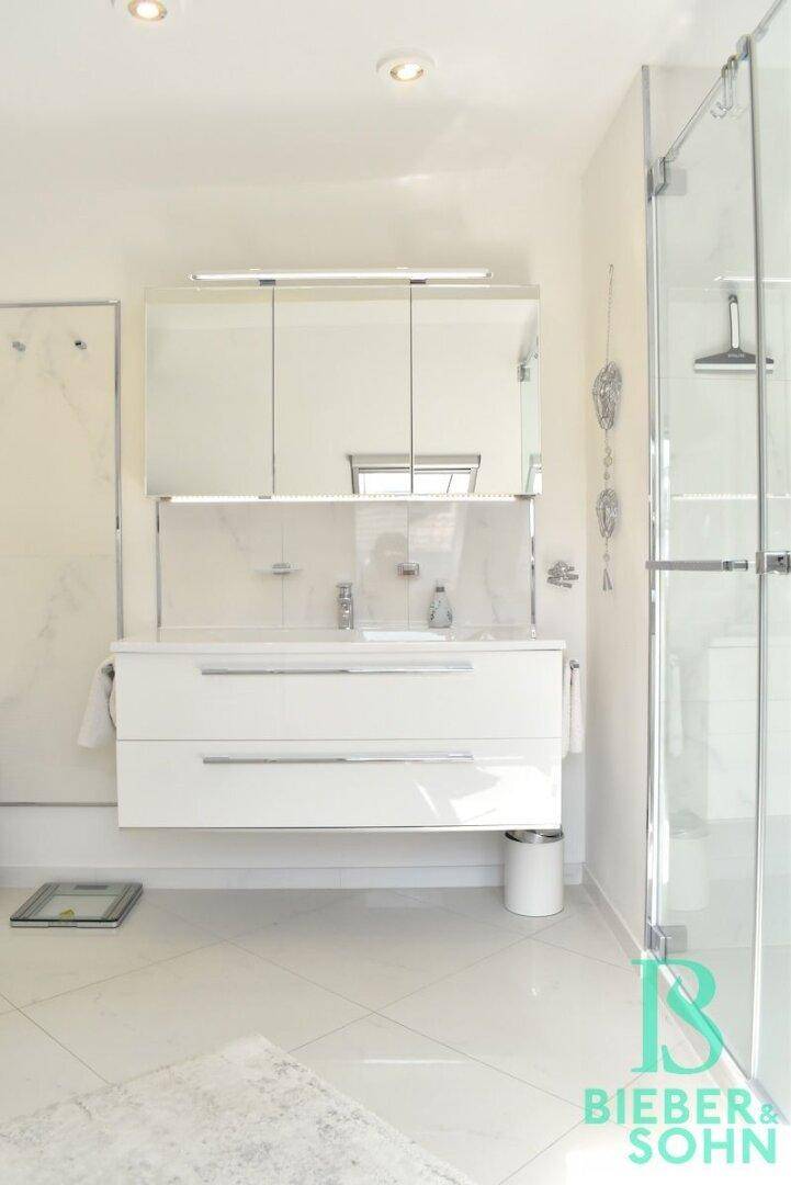Modernes Badezimmer mit weißen Fliesen, schwebendem Waschtisch, Spiegelschrank und Glasdusche.