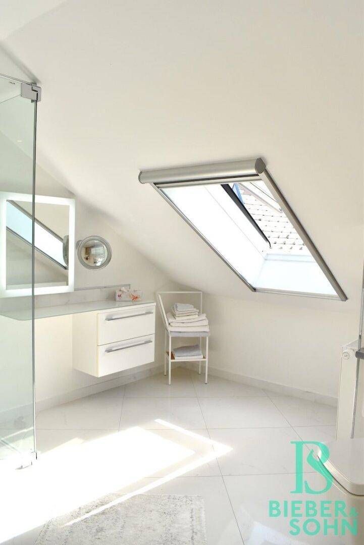 Helles Badezimmer im Dachgeschoss mit modernen Armaturen, weißen Fliesen und einem Dachfenster.