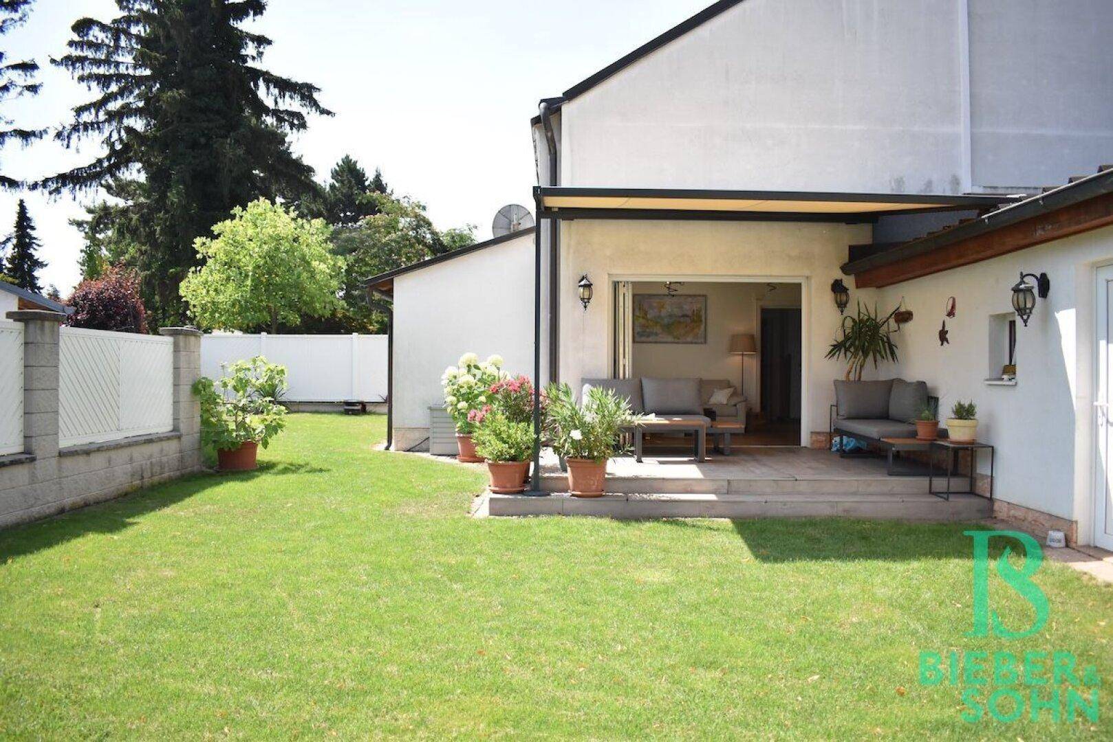 Gepflegter Garten mit Rasenfläche und einer gemütlichen Terrasse mit Sitzgelegenheiten.