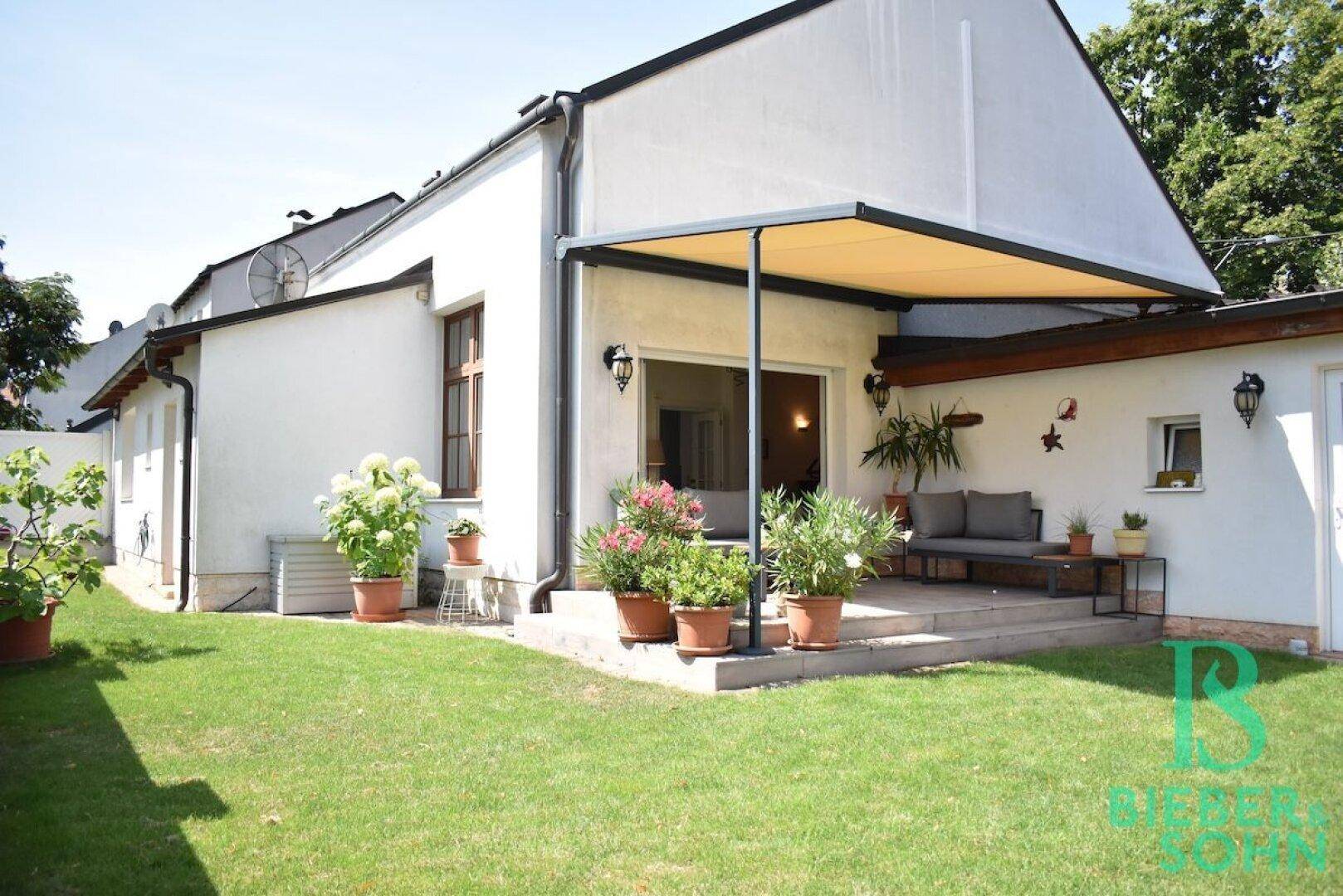 Hausfassade mit überdachter Terrasse, Gartenmöbeln und Blick auf den grünen Garten.