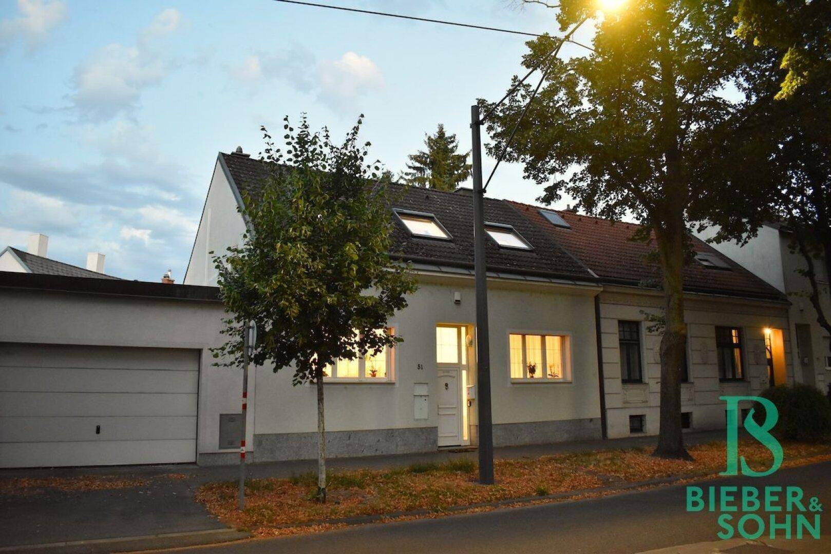 Hausfassade am Abend mit beleuchteten Fenstern und integrierter Garage.