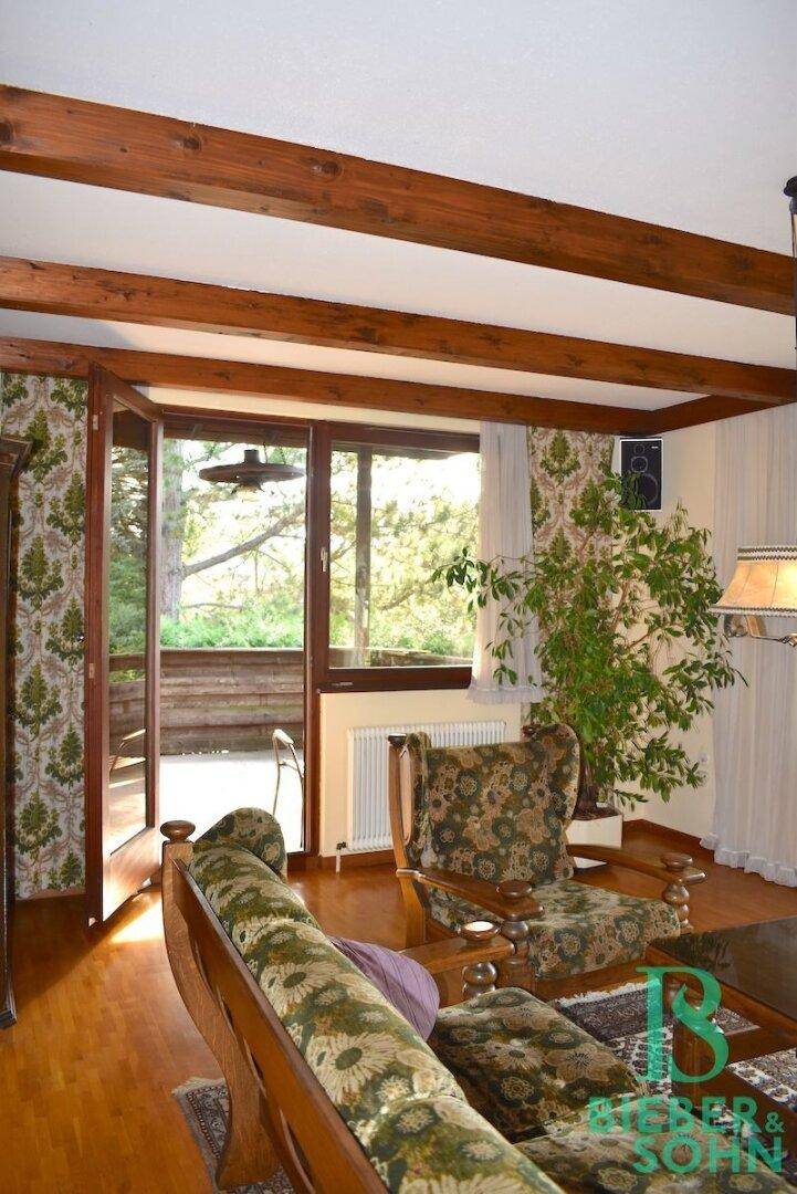 Wohnzimmer mit Zugang zum Balkon, Holzbalkendecke und traditioneller Einrichtung.
