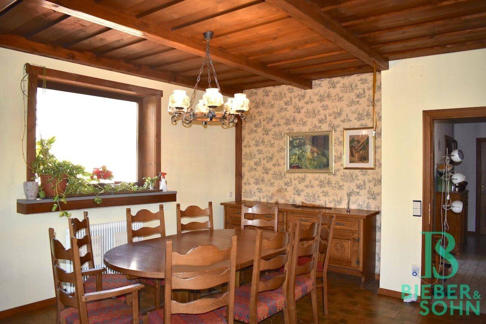 Traditioneller Essbereich mit Holzbalkendecke, großem Esstisch und gemusterter Tapete.