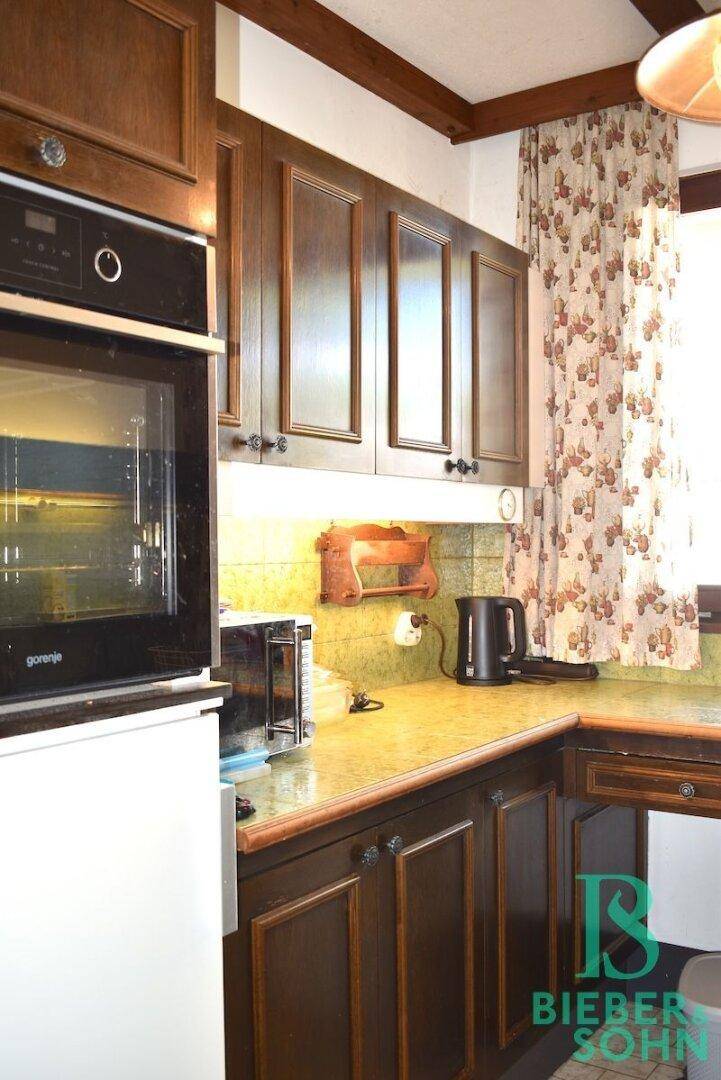 Klassische Küche mit dunklen Holzschränken, integriertem Backofen und Arbeitsplatte.