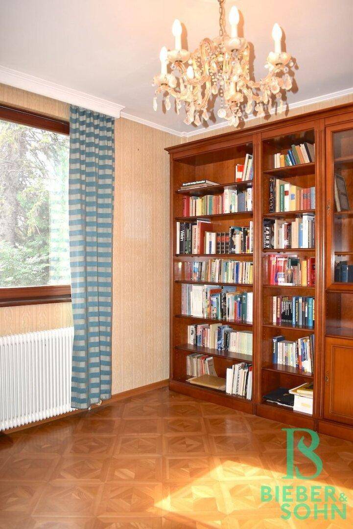Arbeitszimmer mit großem Bücherregal, Parkettboden und Kronleuchter.