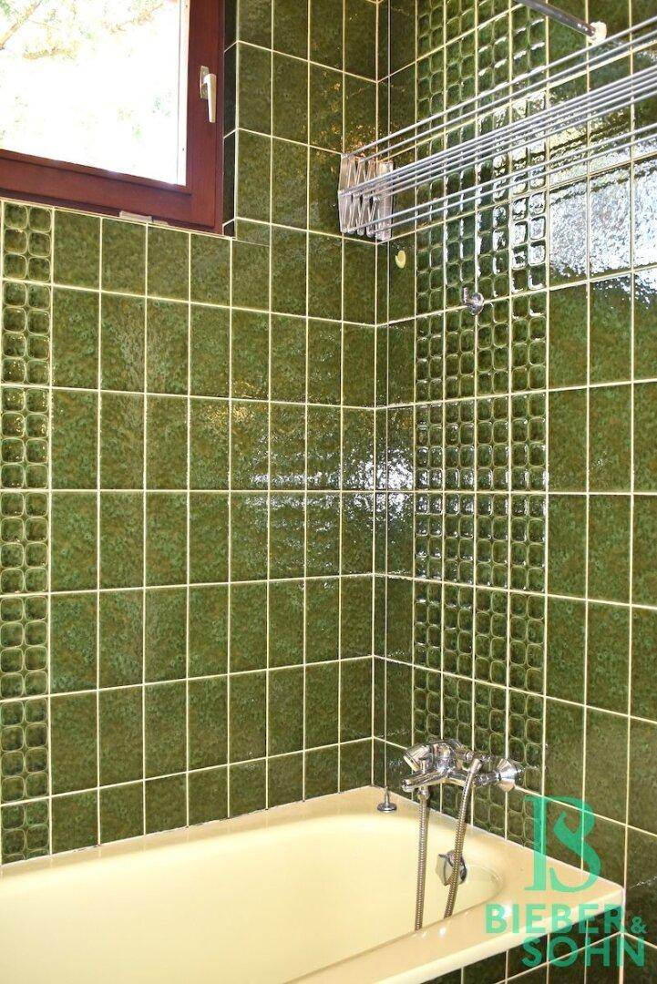 Badezimmer mit grünen Wandfliesen, Badewanne und Fenster.