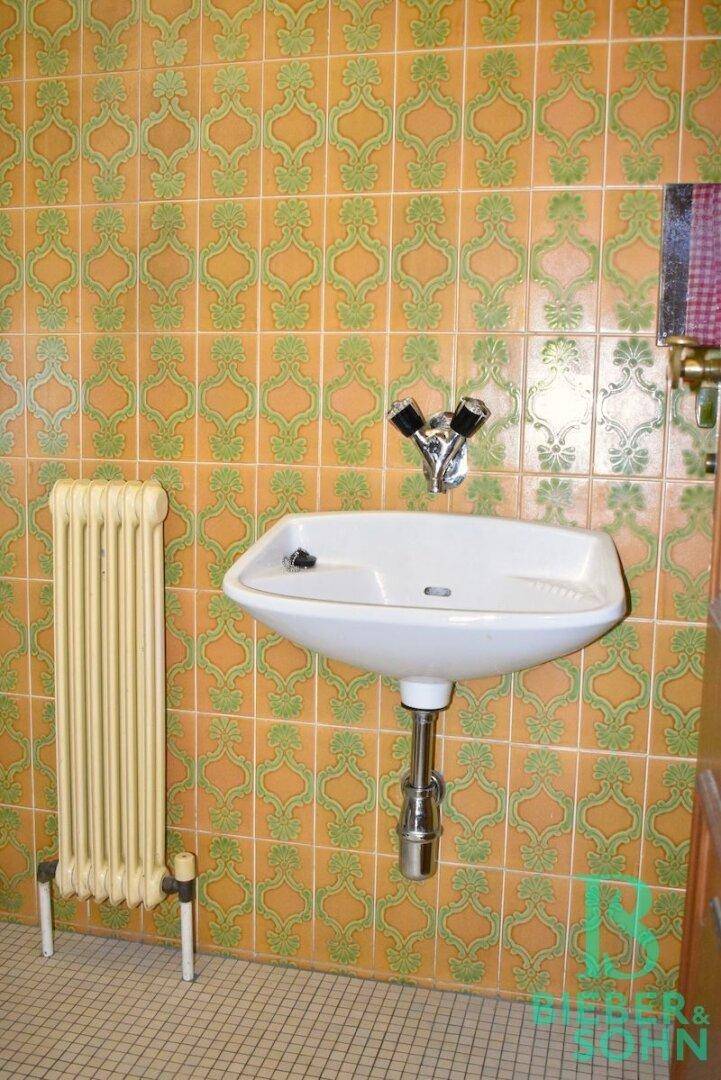 Gäste-WC mit gemusterten Fliesen, Waschbecken und Heizkörper.