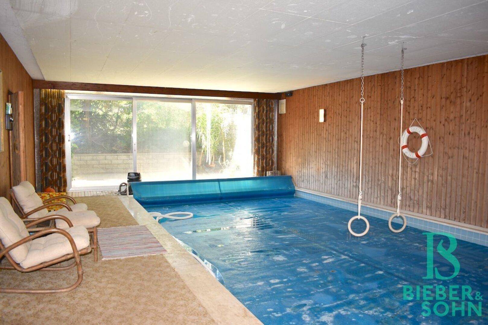 Innenpoolbereich mit Holzverkleidung, großen Fenstern und Sitzgelegenheiten.