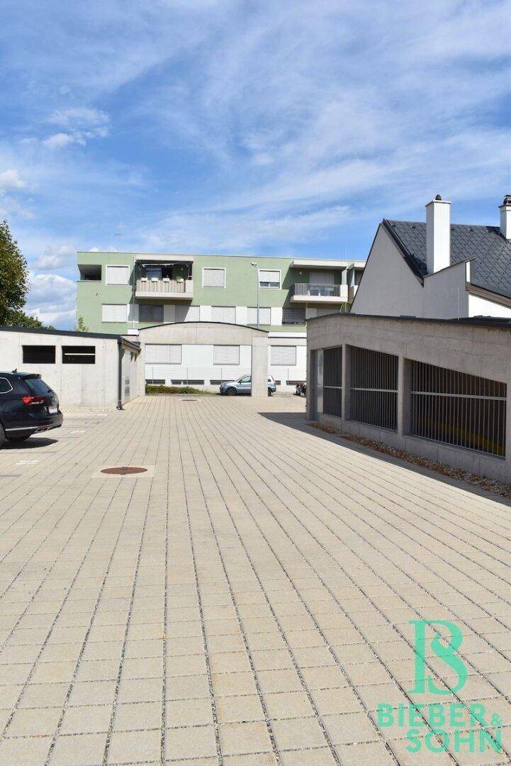 Außenansicht des Gebäudes mit Parkplätzen und umliegender Bebauung unter blauem Himmel.